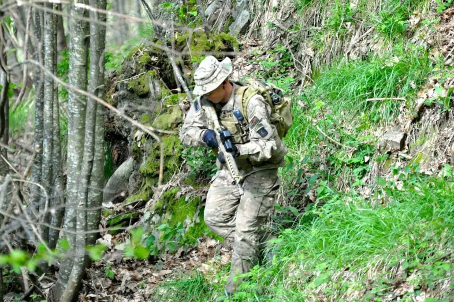 Giocatore softair avanza con cautela lungo un pendio nel bosco