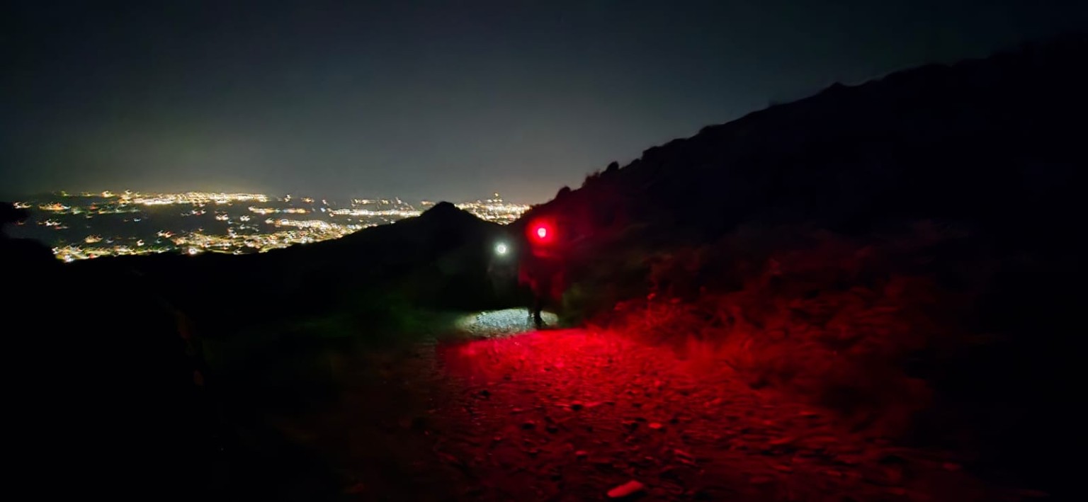 Escursionisti in cammino sul sentiero illuminato da torce bianche e rosse