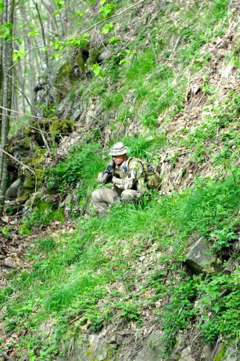 Giocatore softair osserva il terreno dalla vegetazione del bosco